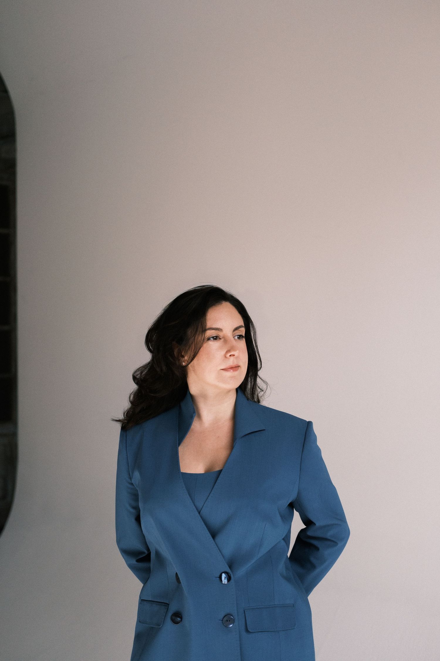 A figure in a navy blue blazer poses against a light gray background in a dynamic fashion series.