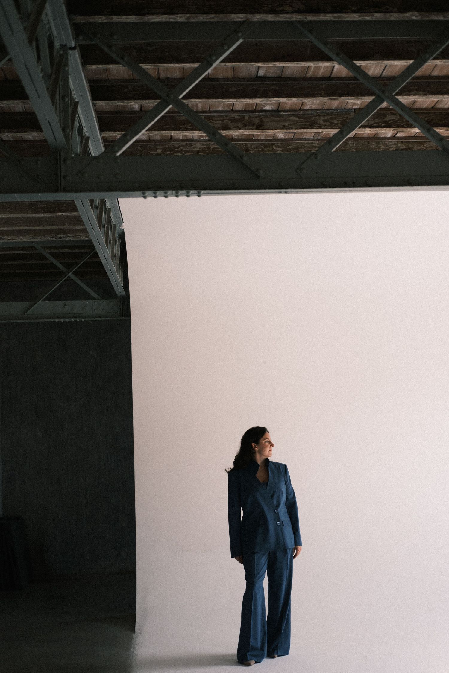 A sequence of minimalist photos showing a blue dress against a white wall in an industrial space with exposed beams.