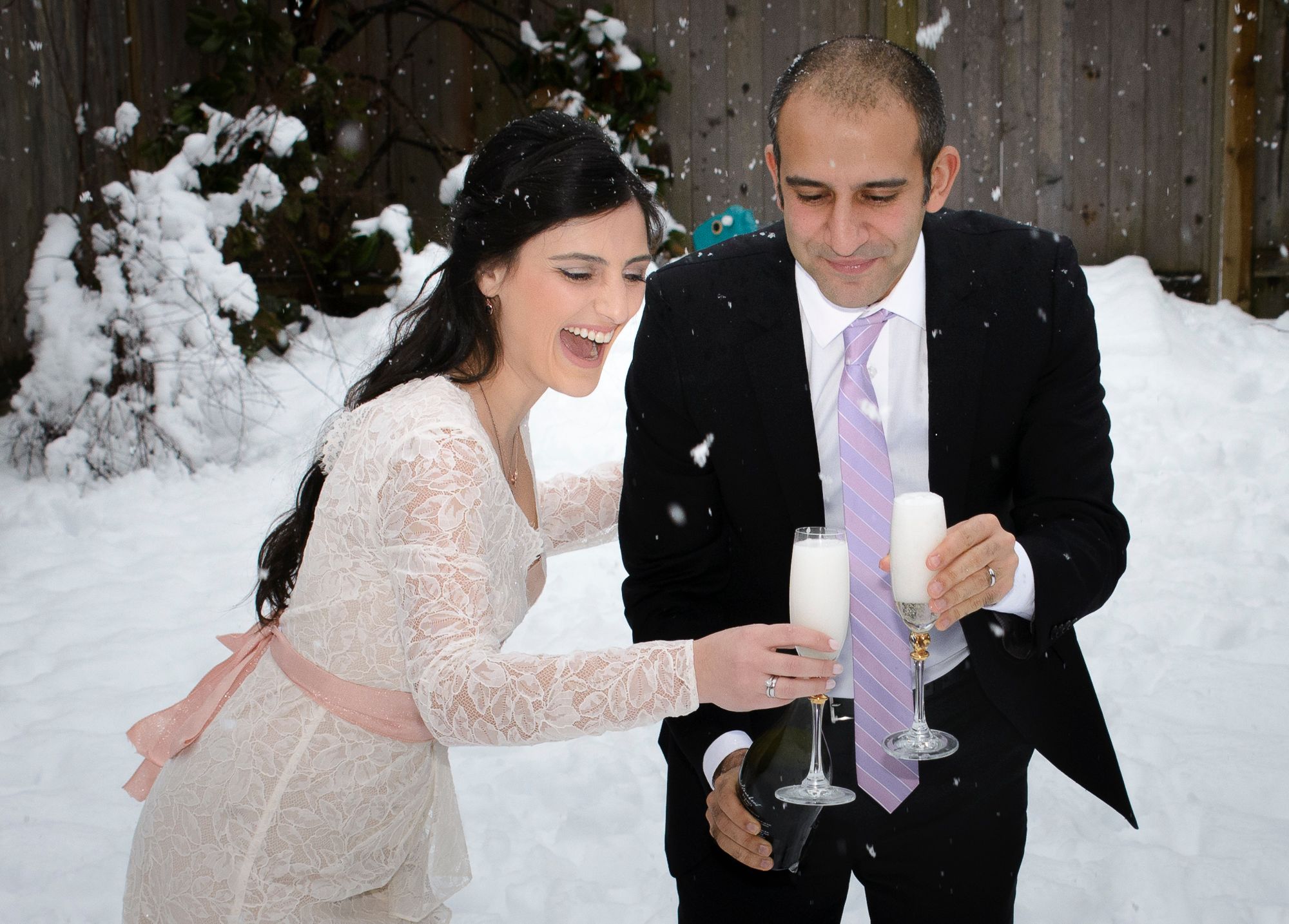 A couple in wedding attire playfully enjoying a snowy winter day during their outdoor photo session.