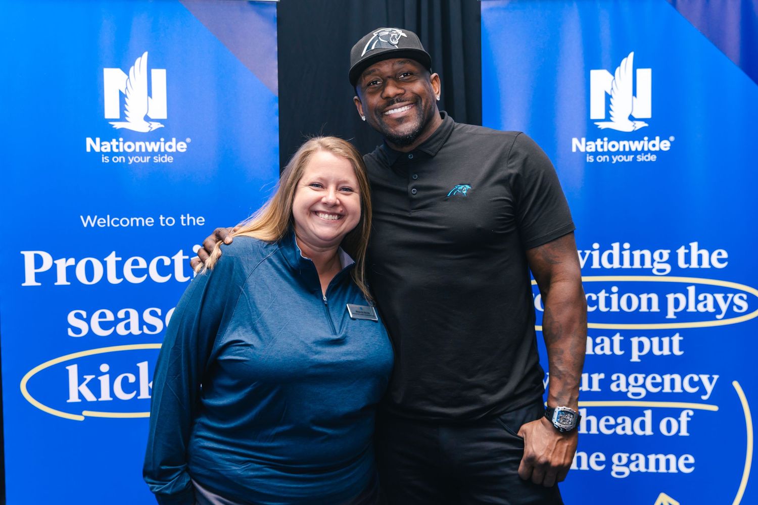 A woman in a blue polo poses with a man in a black cap at a Nationwide event.
