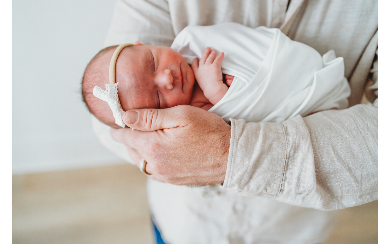 Newborn baby wrapped in white swaddle being held gently.