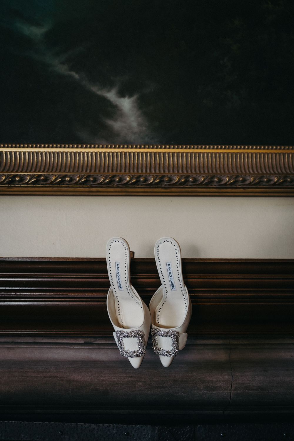 Elegant white bridal shoes with crystal embellishments displayed against a dark wooden floor.