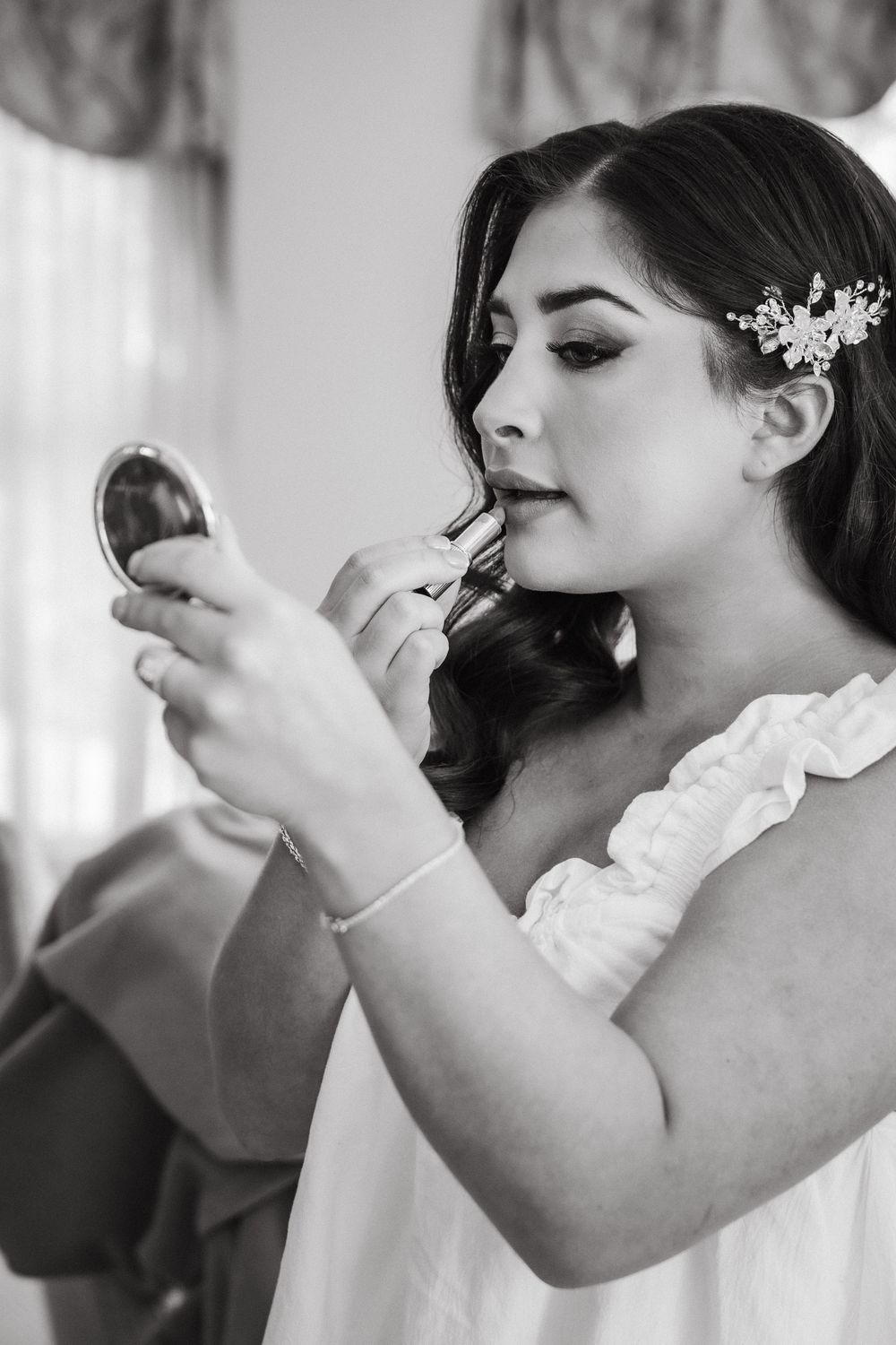Black and white photo showing the application of makeup during wedding preparations.