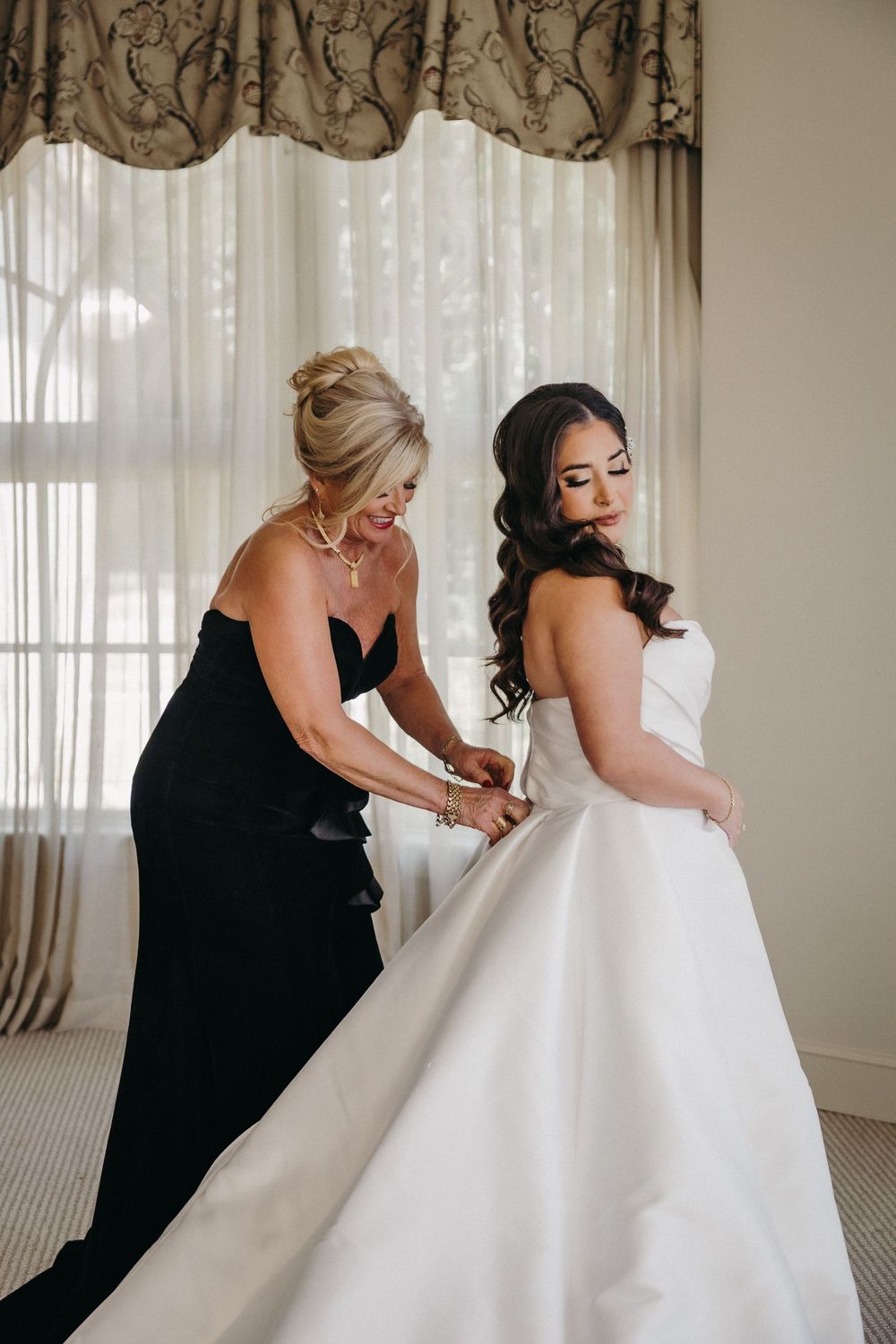 Wedding dress preparation scene with bridesmaids in black helping with the white gown.