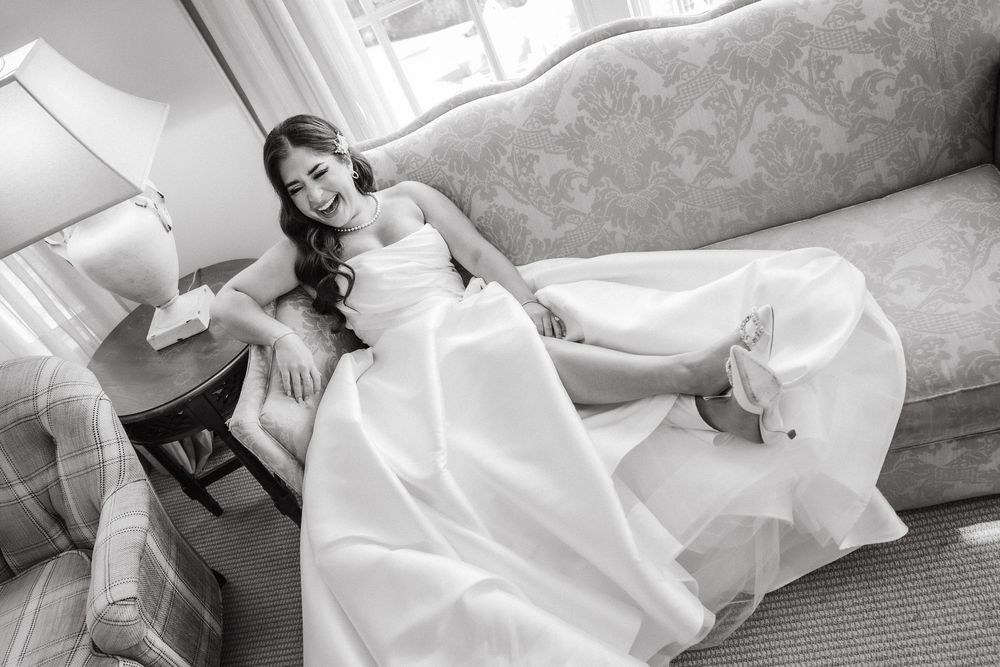 Bride in white dress reclining on elegant furniture during wedding preparation.