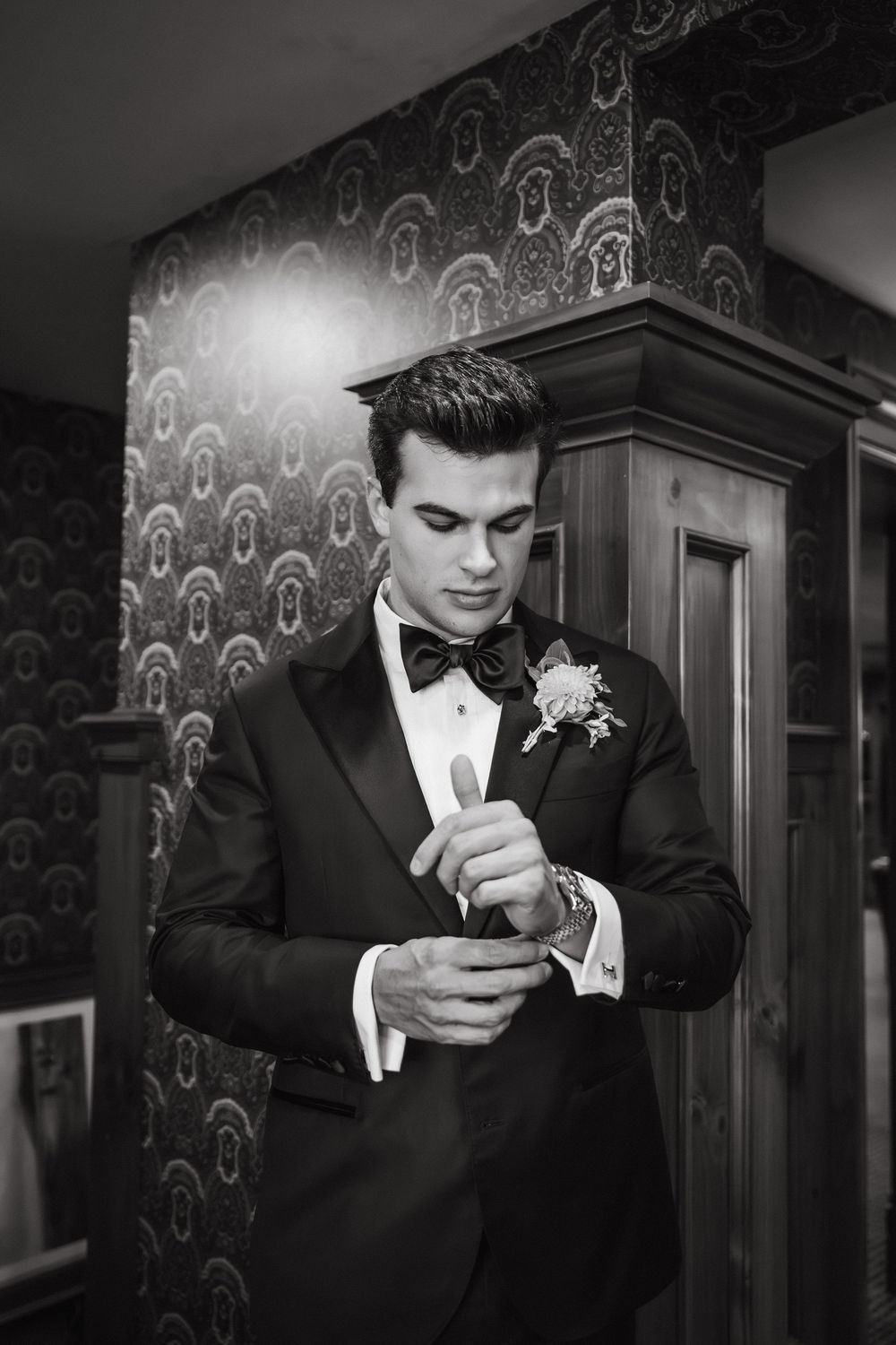 Close-up shots of groom adjusting his tie against ornate wallpaper background.