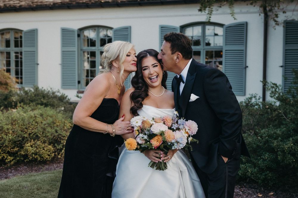 Wedding party posing outdoors with colorful bouquets against white building backdrop.