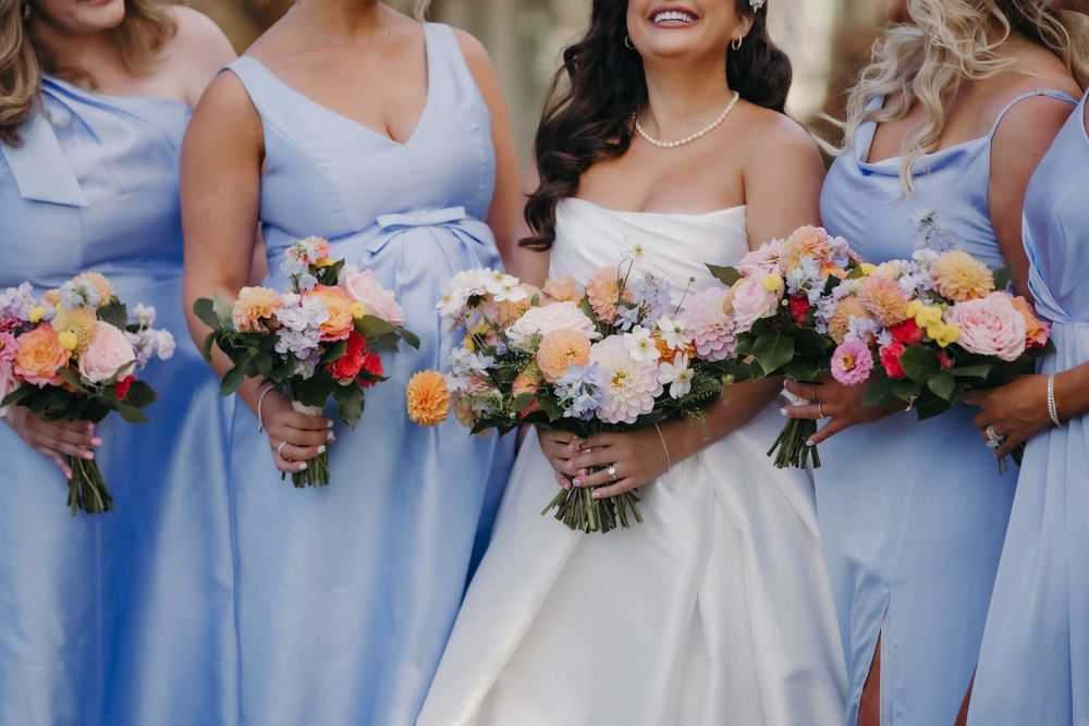 Bridesmaids in light blue dresses holding colorful floral bouquets.