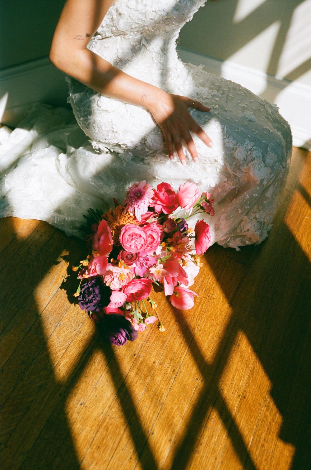 Pink and coral flowers scattered on a wooden floor next to the hem of a white wedding dress.