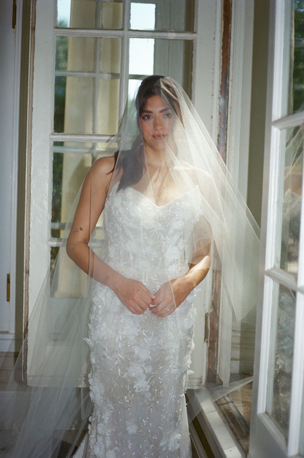 A dreamy bridal portrait through sheer white veil material framed by window panes.