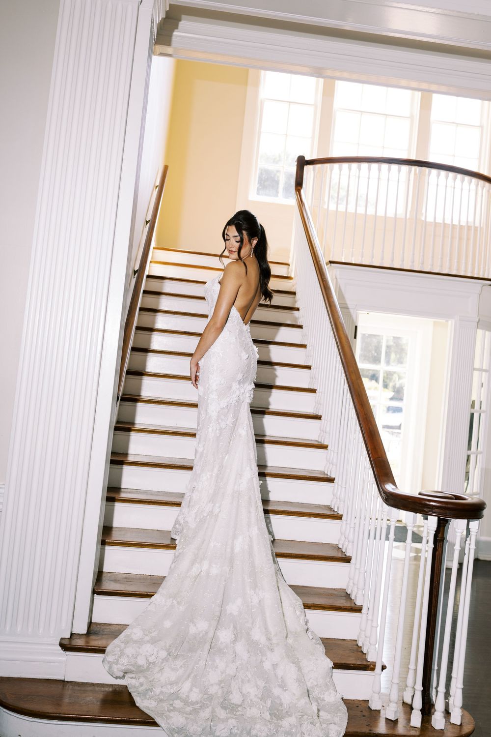 Elegant wedding dress with lace train photographed on classic white staircase.