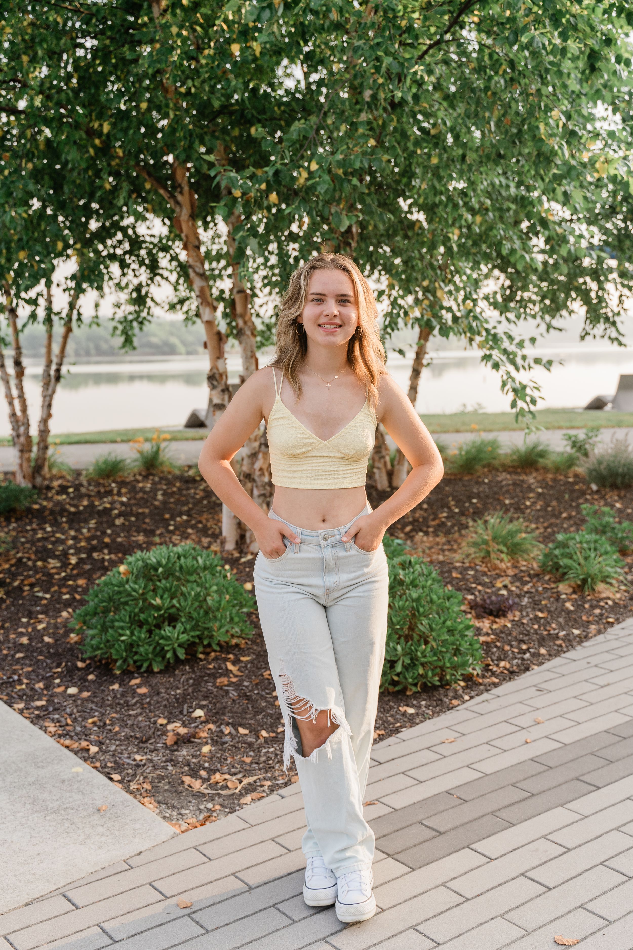 A series of five photos showing someone in light blue jeans and a white top posing casually on a paved walkway near landscaping.