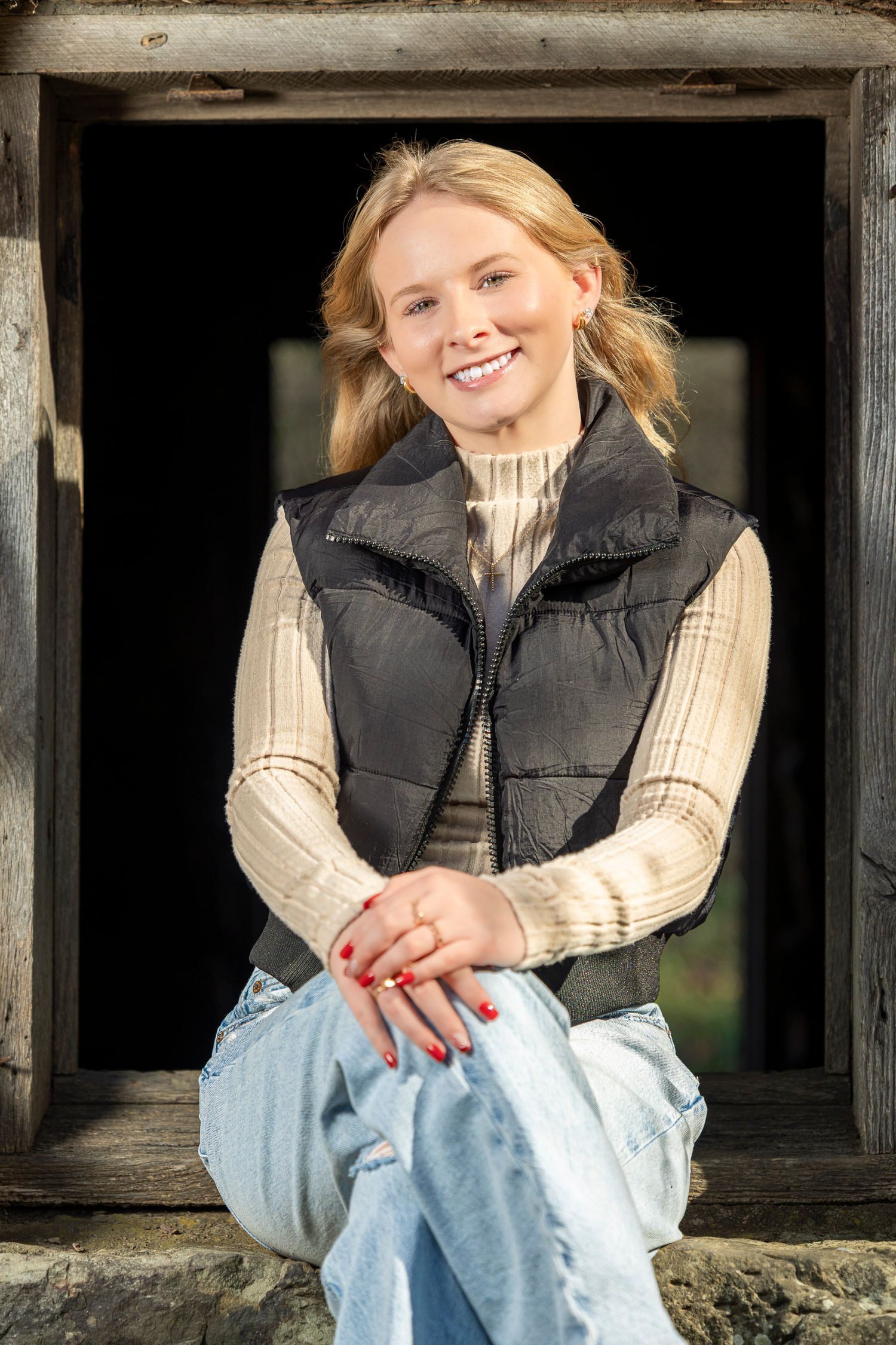 Person wearing black puffer vest and cream sweater sits in rustic wooden window frame.