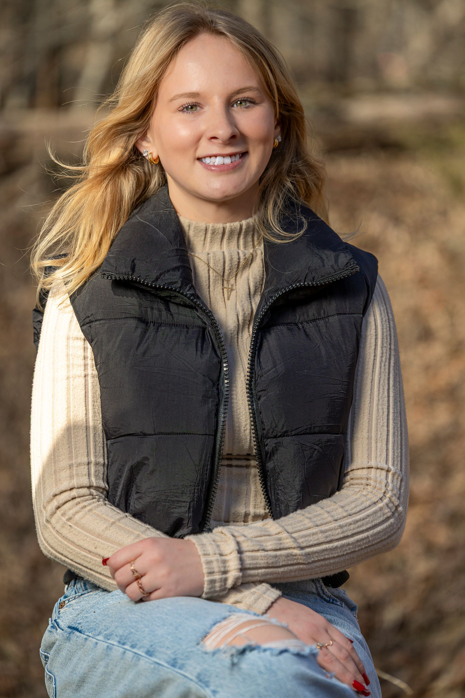 Woman in black puffer vest and beige sweater poses outdoors in casual winter attire.