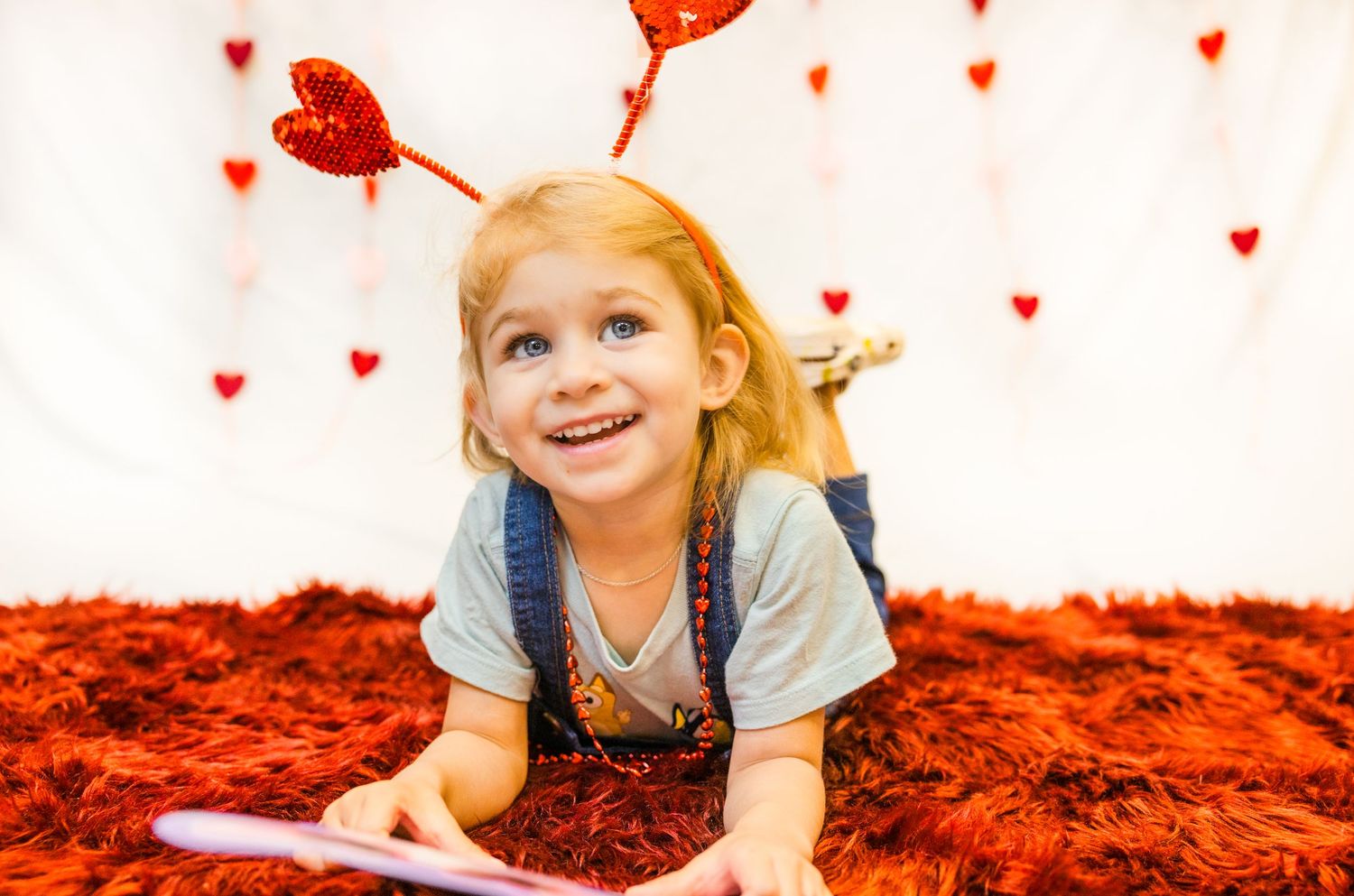 Photo showing someone lying on a red fluffy carpet with scattered heart decorations.