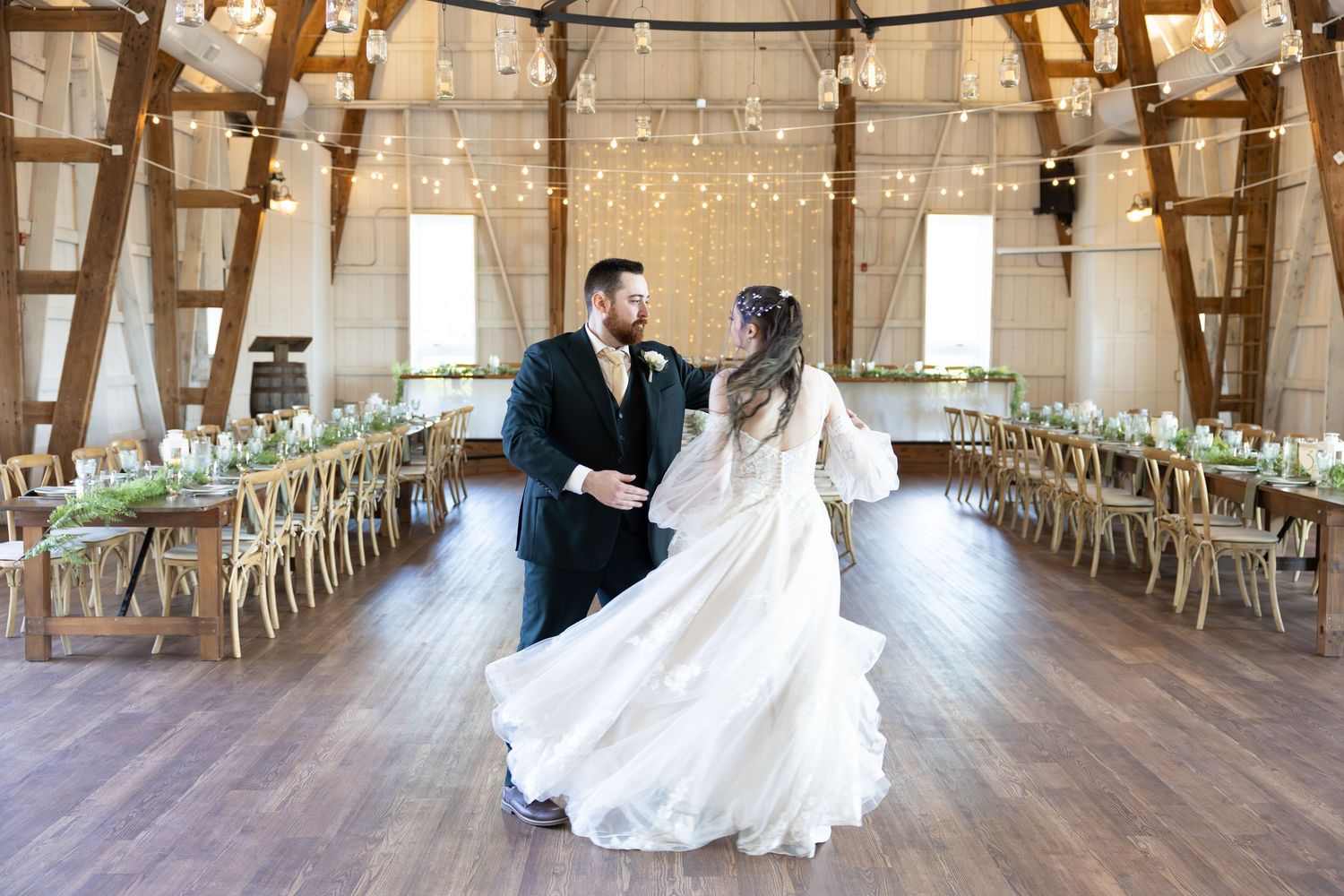 Rustic barn wedding venue decorated with string lights and wooden chairs arranged in rows for a ceremony.