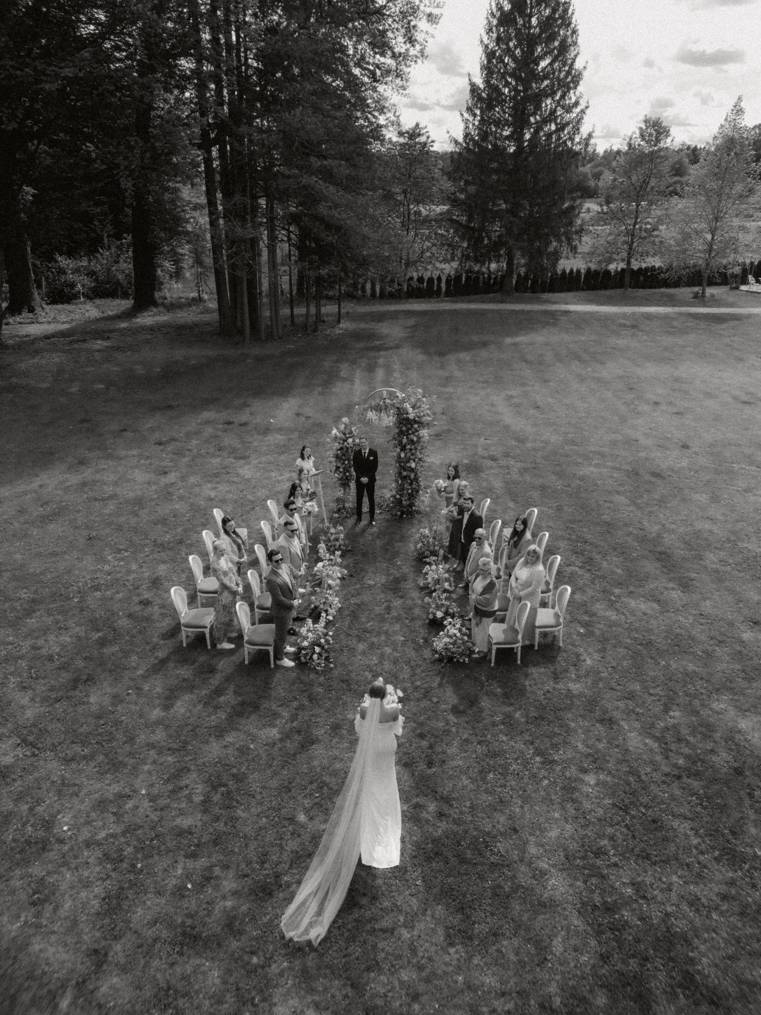 Aerial view of an outdoor wedding ceremony with guests seated in a unique arrow formation.