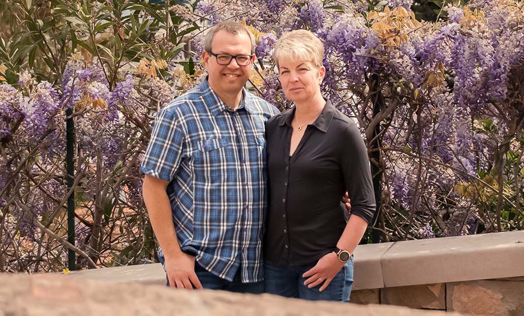 Outdoor-Paarportrait vor blühenden Sträuchern, natürliches Lächeln und entspannte Pose im Garten