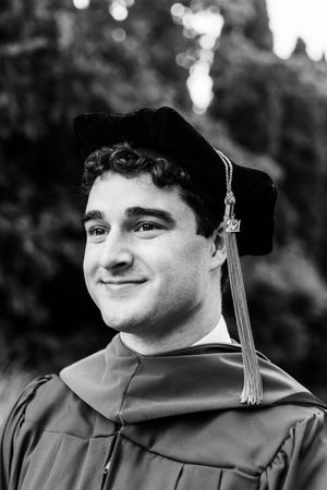 Black and white portrait of graduate in academic regalia with tassel and hood during graduation ceremony.