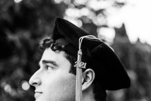 Black and white profile portrait of a graduate in cap with tassel against a blurred outdoor background.