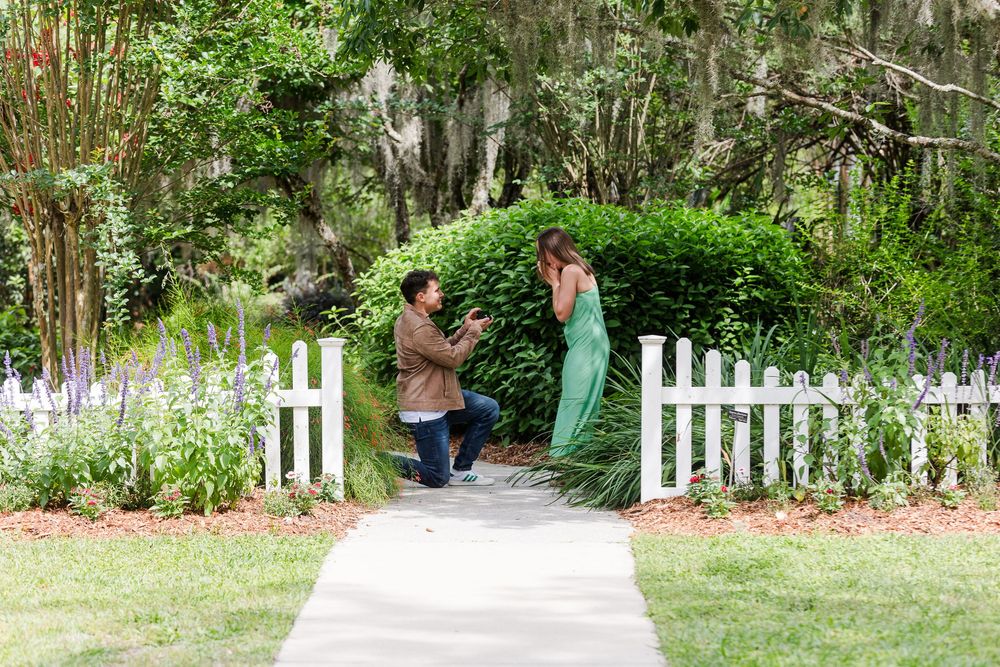 A couple shares a special moment on a garden path with white picket fence and Spanish moss draped trees in background.