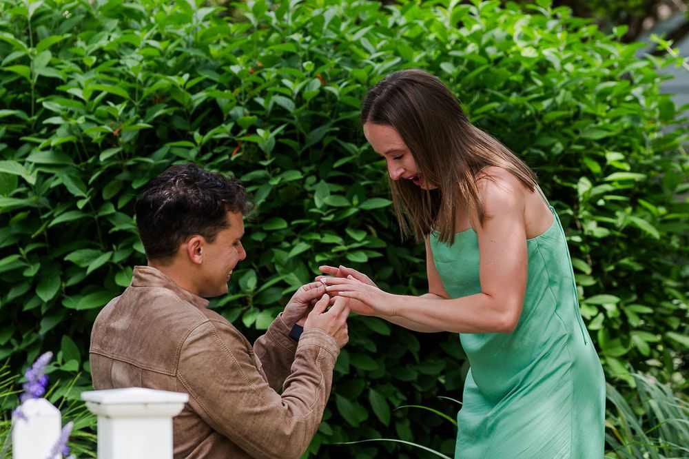A couple in brown and green outfits shares a tender moment while dancing together in a lush garden setting.