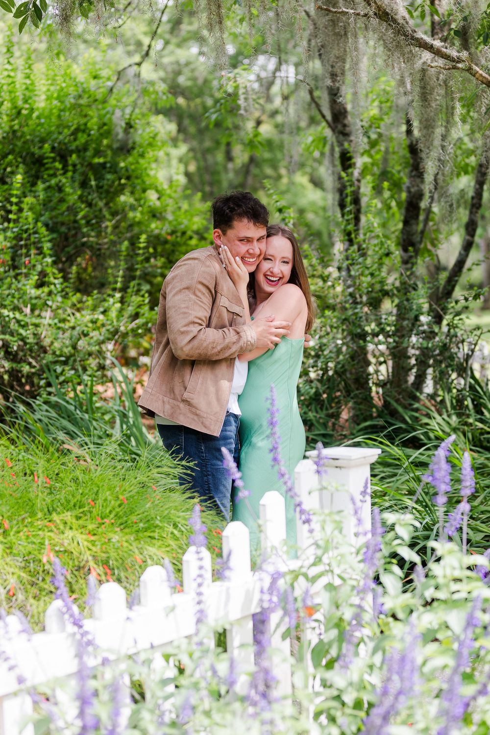 Couple shares romantic moments among blooming purple wildflowers in a lush garden setting.