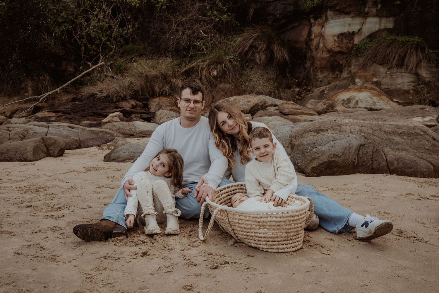 Family portrait session on a sandy beach with a baby in a vintage-style basket near by during a central coast family photoshoot.