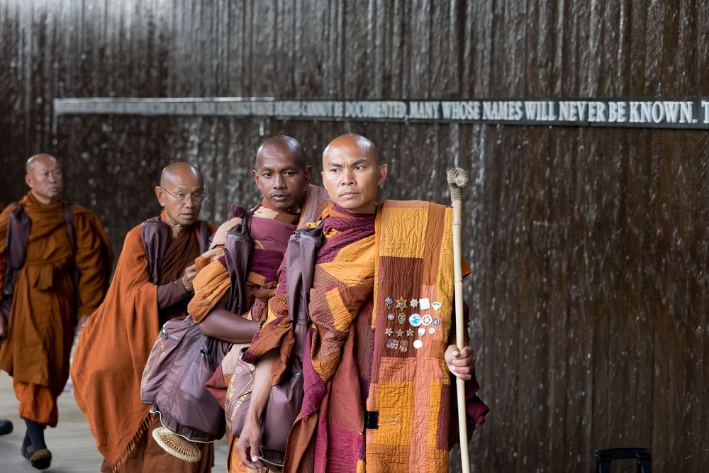 Buddhist monks in traditional orange robes gather together in front of a wooden wall.