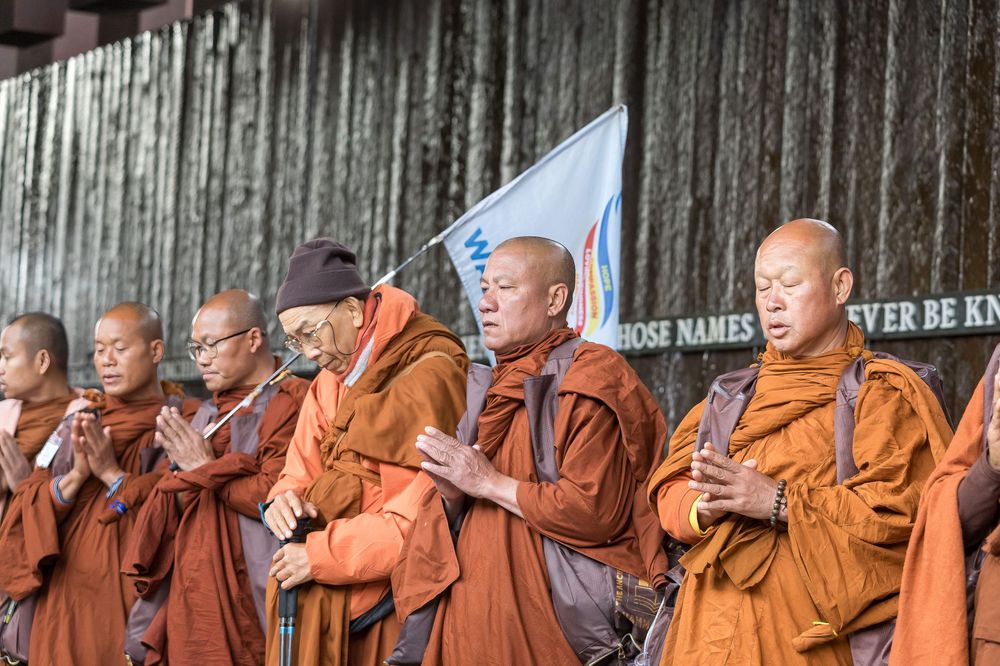 Buddhist monks in orange robes stand in a row during a ceremony or gathering at a temple.