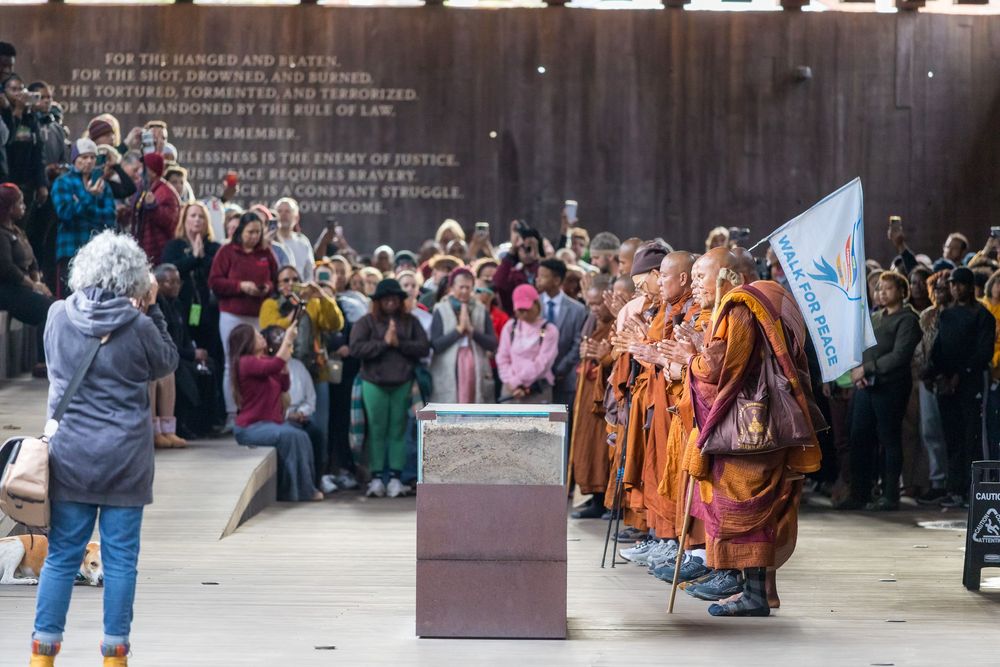 A group of tourists gather around a memorial or monument site while guides provide information and interpretation.