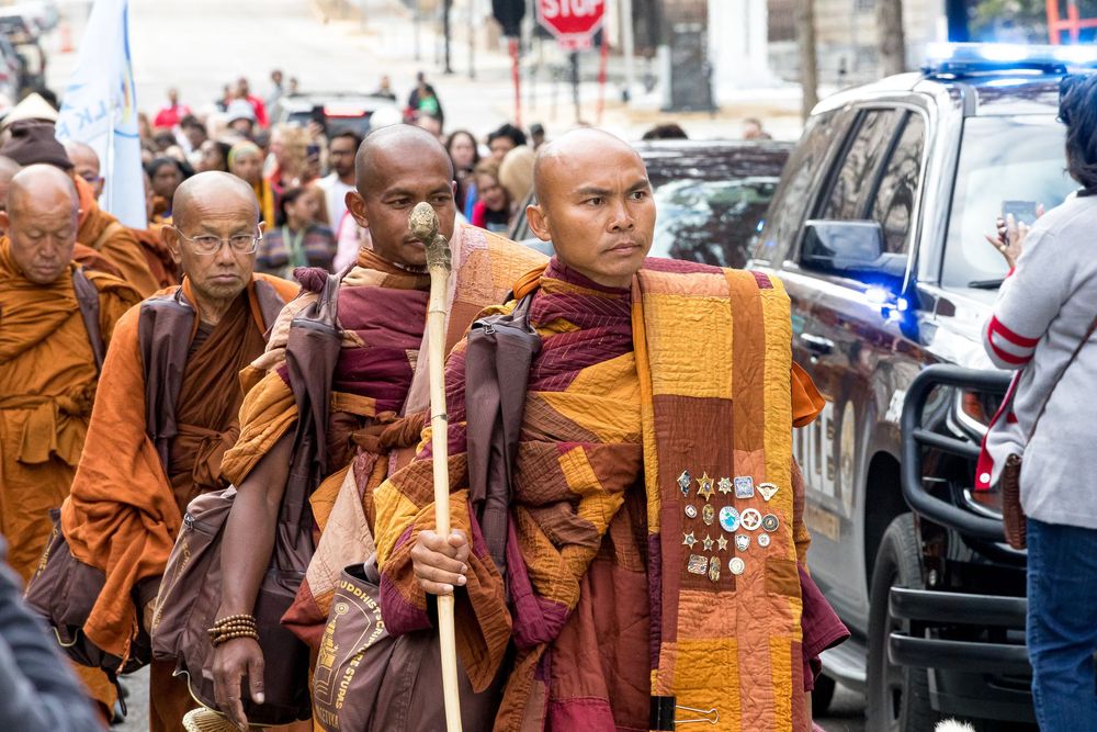 Buddhist monks in traditional saffron robes walk in procession through a busy city street.