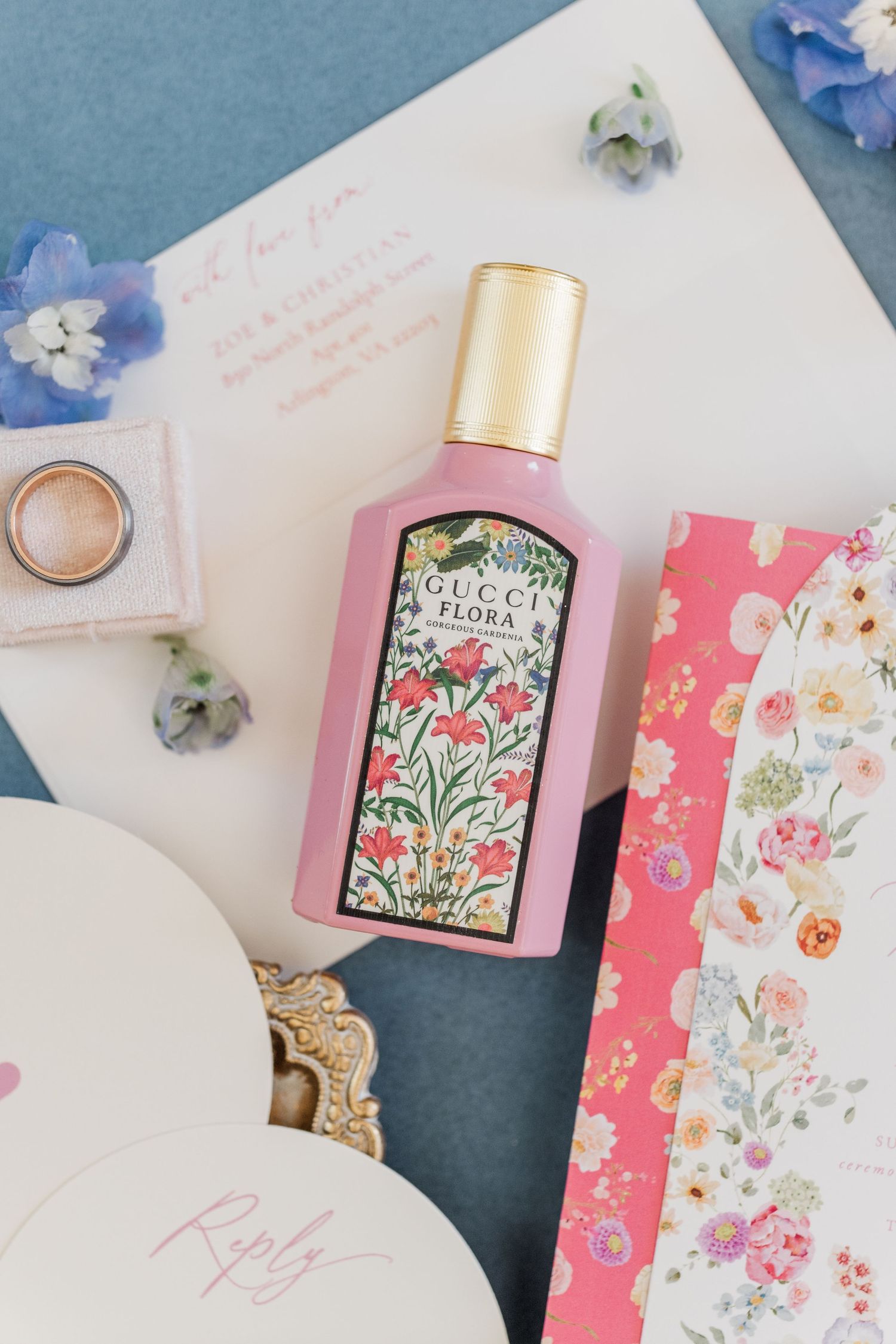 Wedding stationery with floral designs and a pink perfume bottle on blue background.