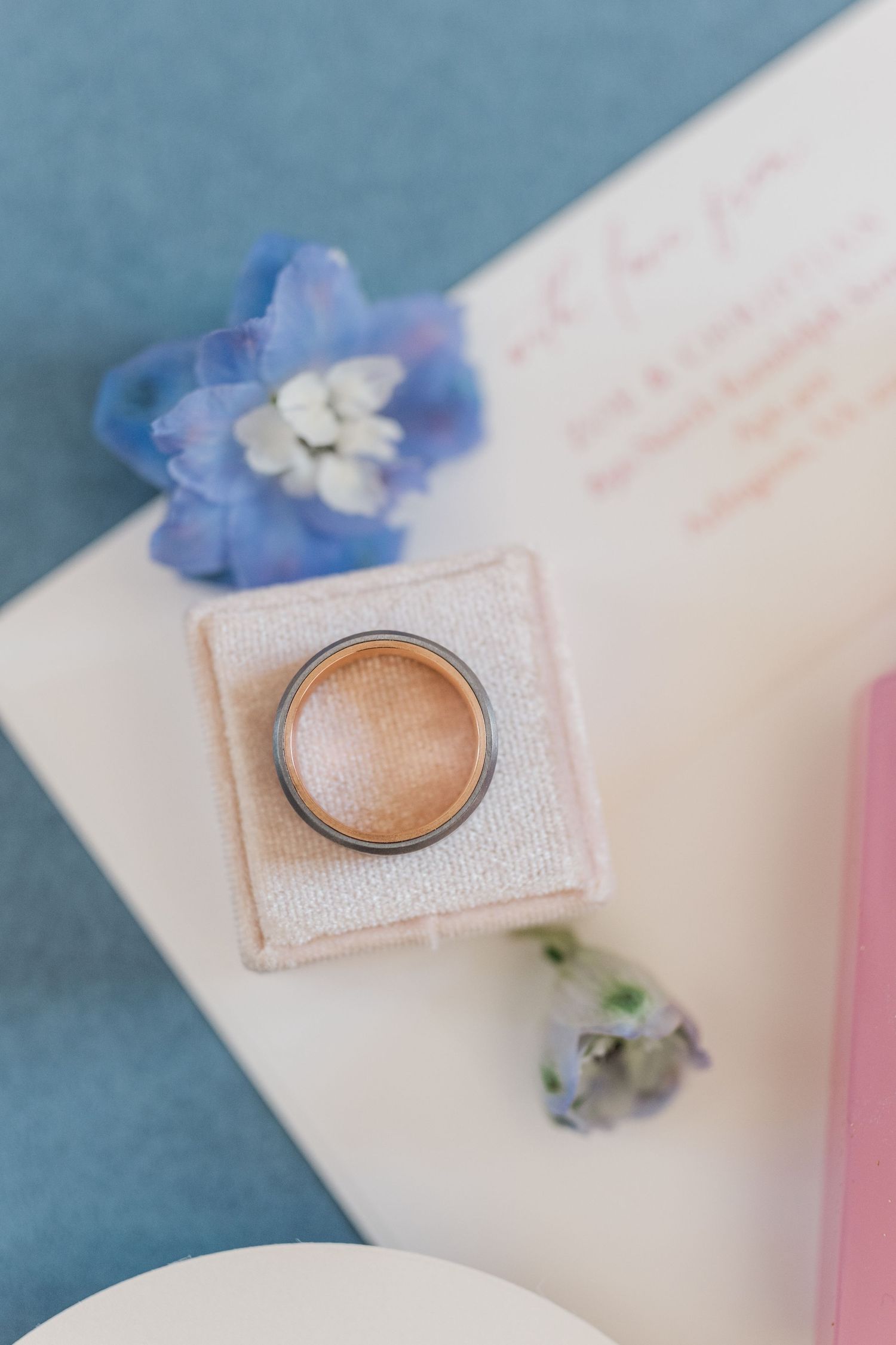 Wedding ring displayed with delicate blue flowers on white surface.