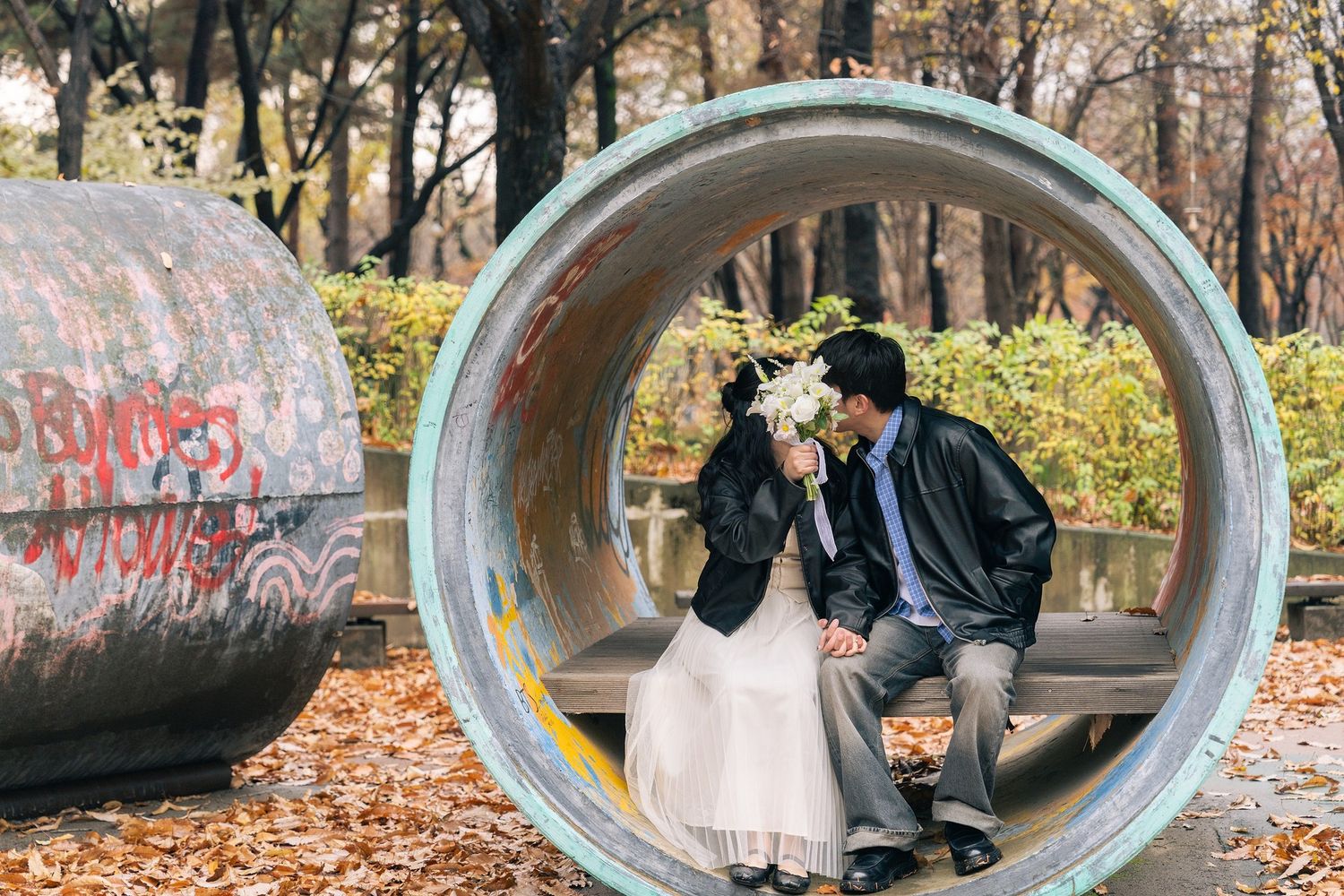 A romantic autumn scene inside a large concrete pipe with fallen leaves and trees in the background.