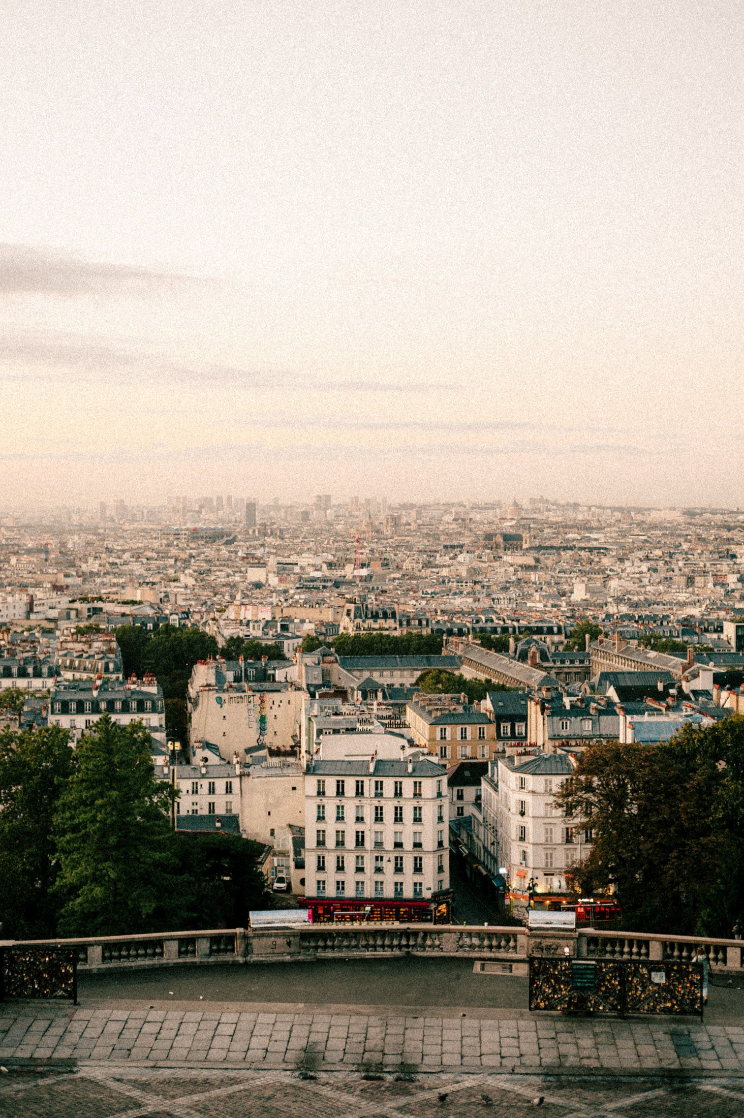 Panoramic cityscape view of Paris from Montmartre showing historic buildings and rooftops at sunset.