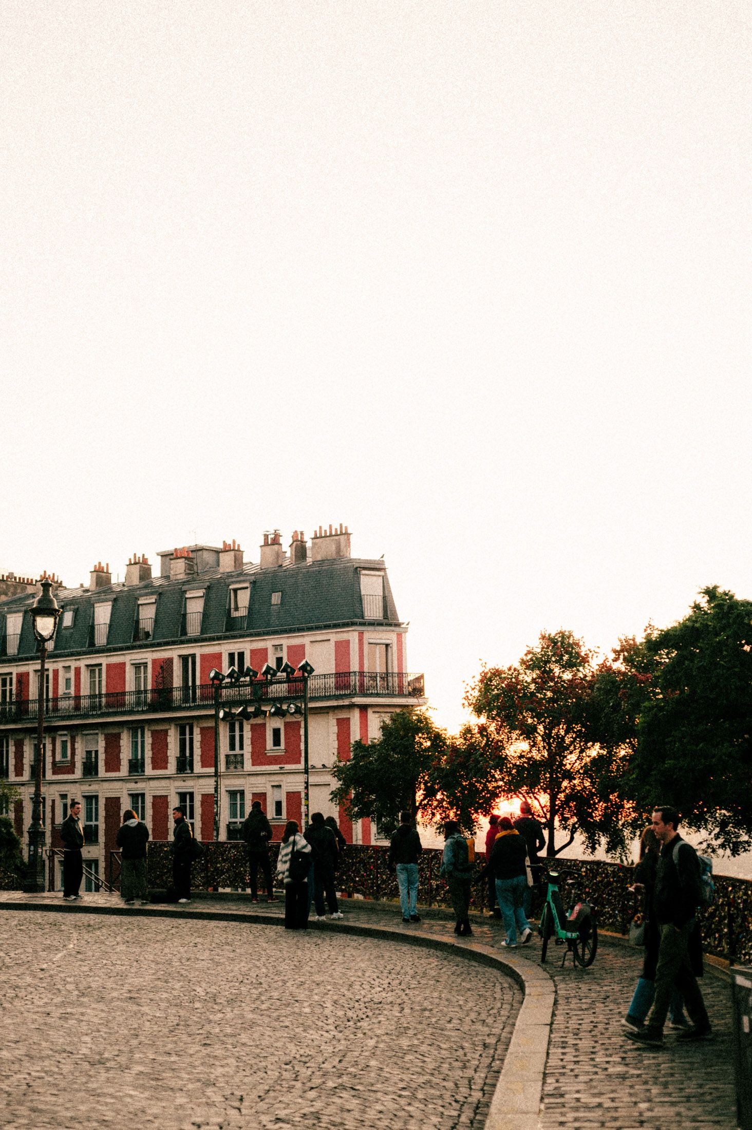 Historic Parisian building with mansard roof and cobblestone street at sunset with people strolling along the path.