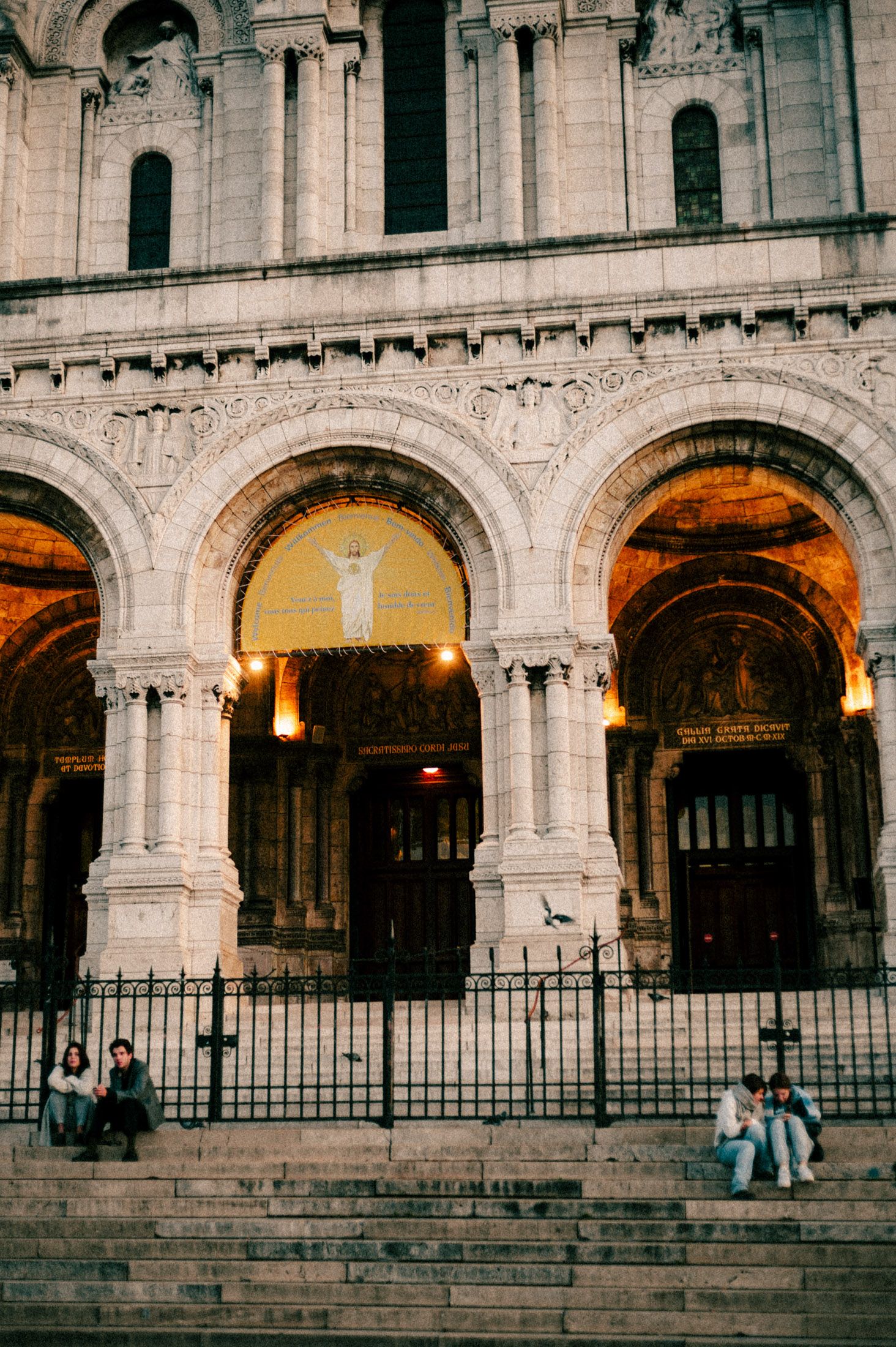 Ornate stone arches and columns of a historic European building facade illuminated by warm evening light.