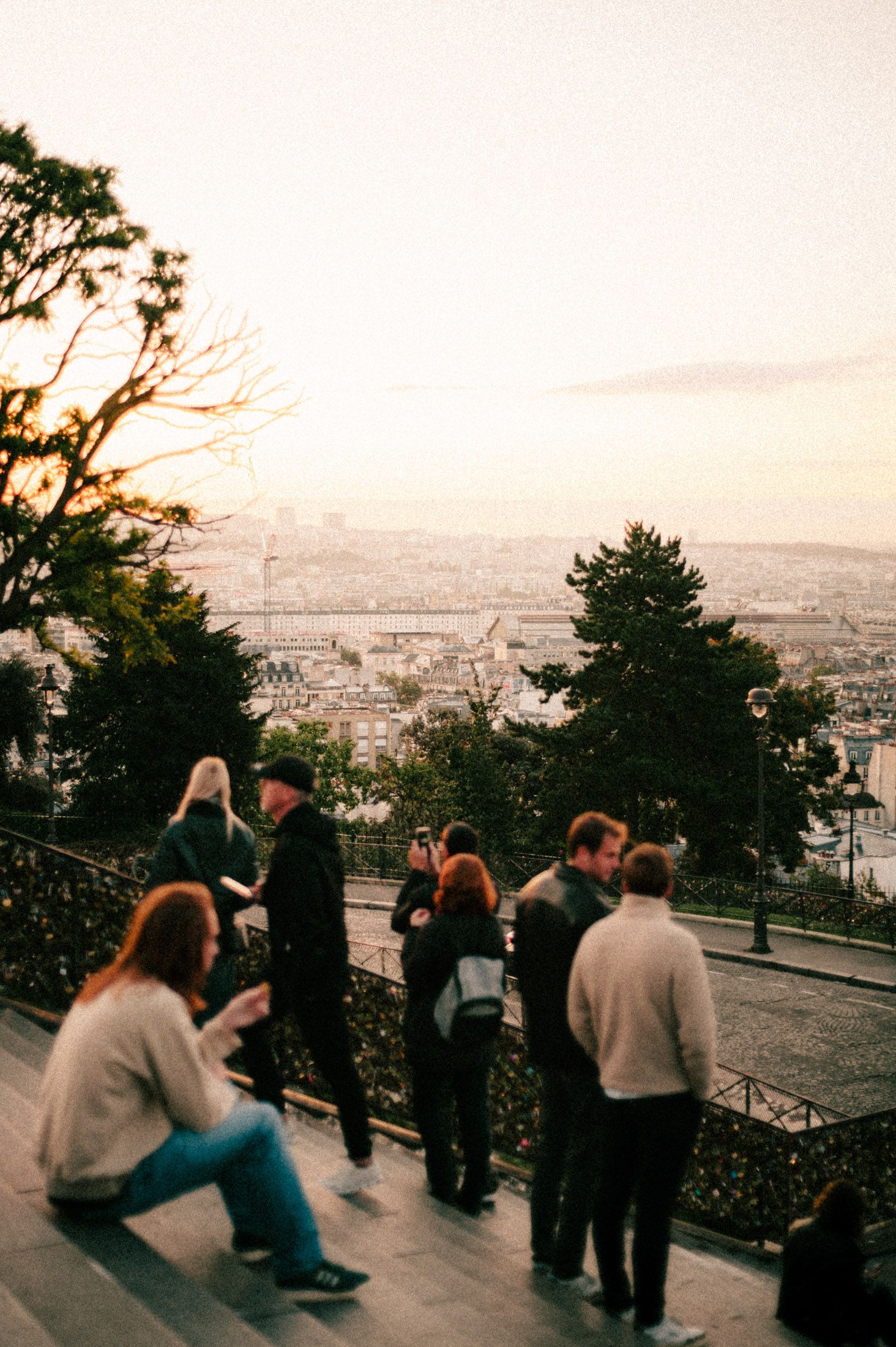 Tourists gather at a scenic overlook in Paris during sunset, offering panoramic views of the cityscape below.