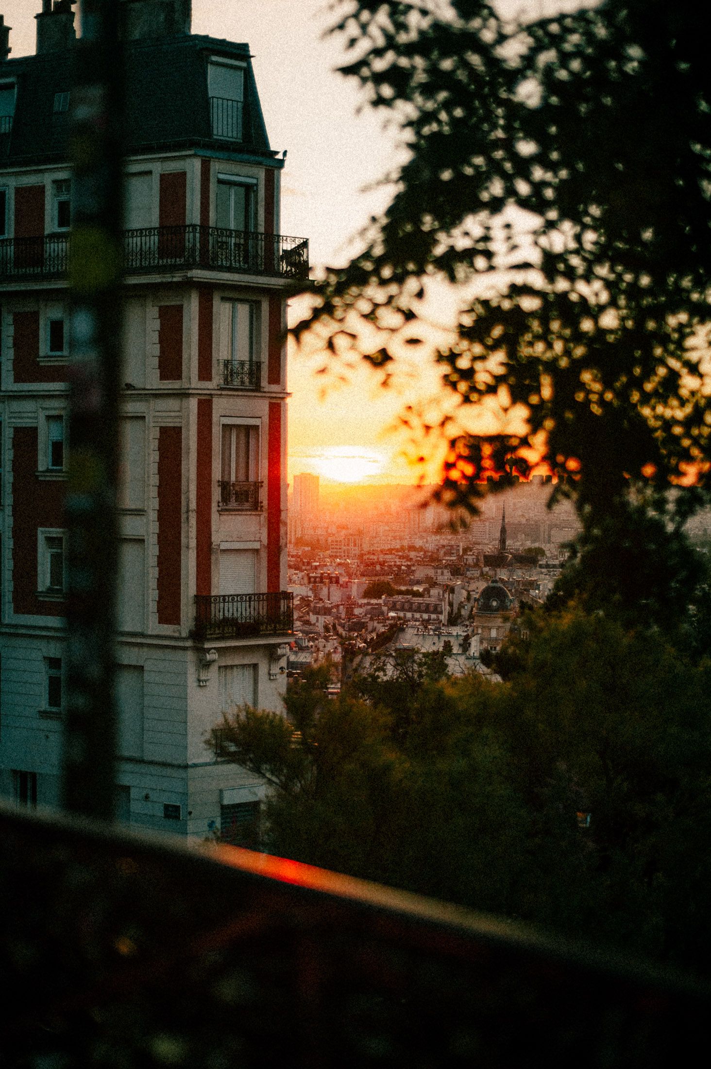 Sunset view over Paris cityscape with historic apartment buildings silhouetted against an orange sky.