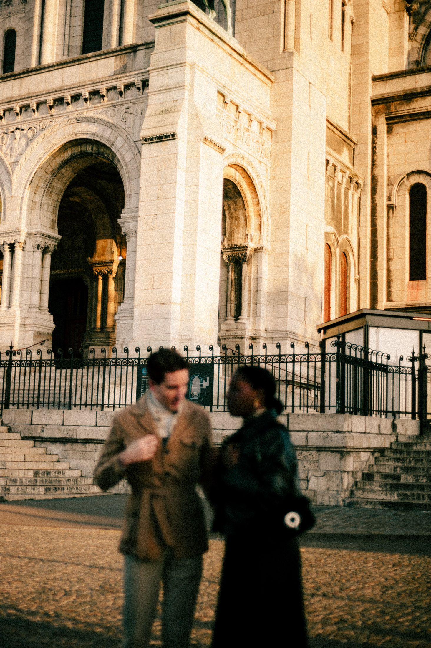 Gothic architecture of Sacre-Coeur Basilica in Paris with visitors on the cobblestone plaza at golden hour.