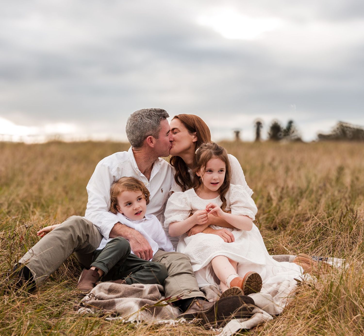 Family lounging together in grassy field during golden hour.