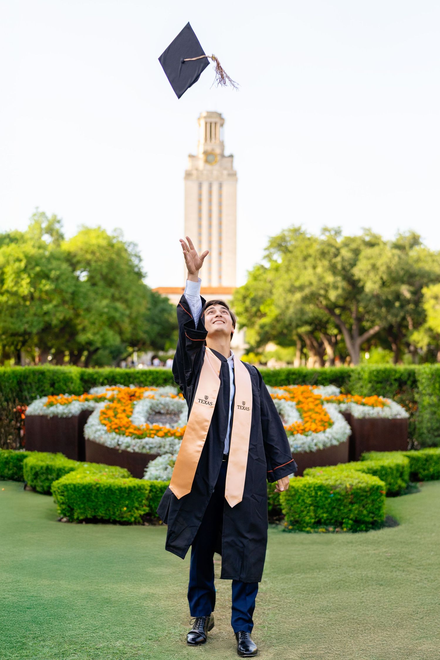 Graduate in black cap and gown throws graduation cap in the air during outdoor ceremony celebration at university campus.