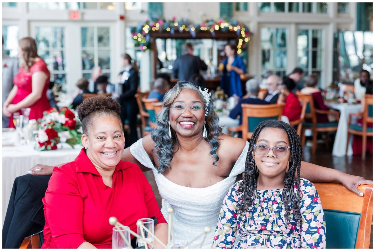 Reception guests gather at decorated tables in bright sunlit venue with festive holiday decor.