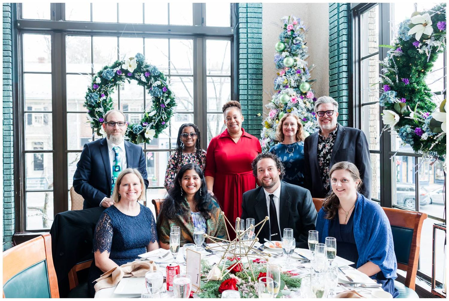 A festive holiday gathering around an elegantly decorated dining table with wreaths and Christmas decor in the background.