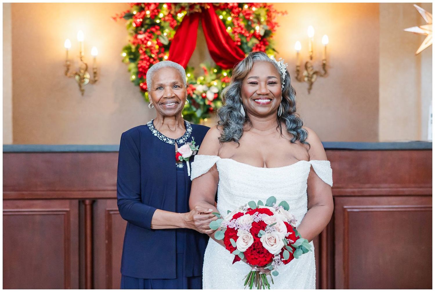 Wedding party poses with red and white floral bouquets in an elegant venue with ornate wall sconces.