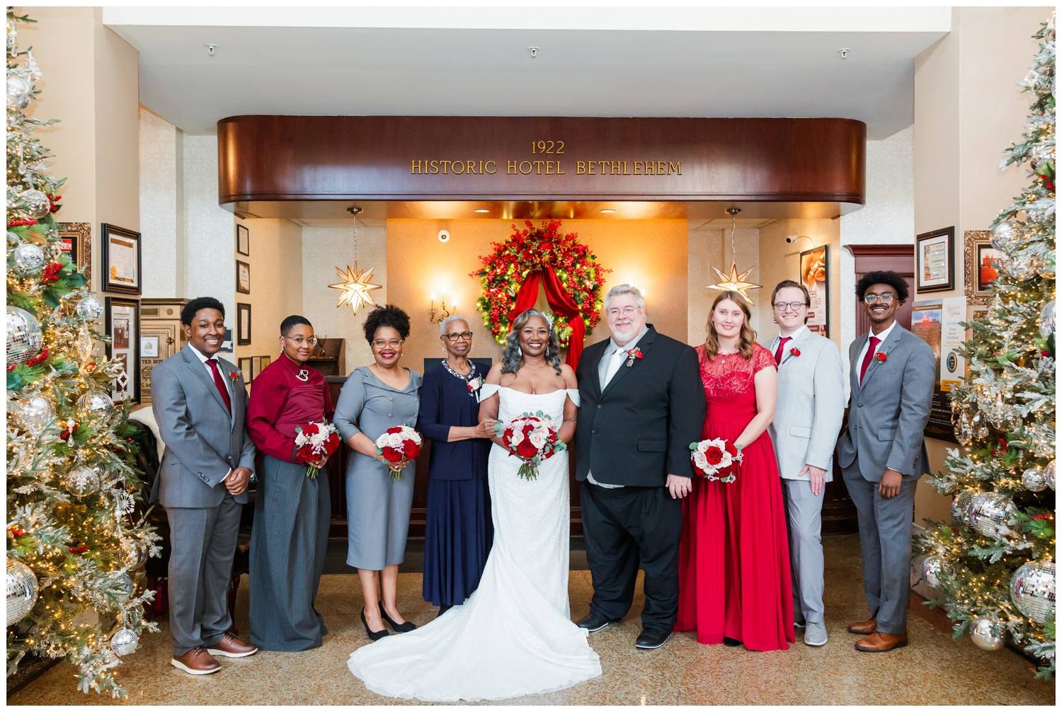 Wedding group photo lineup against cream walls with elegant floral arrangements and holiday decorations.