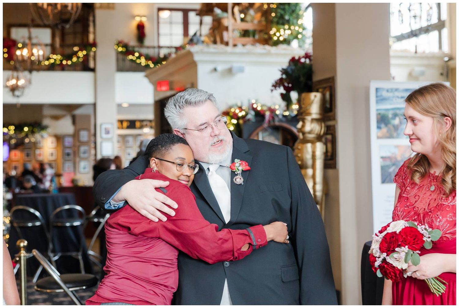 Wedding party members share joyful embraces and greetings in a warmly lit indoor venue.