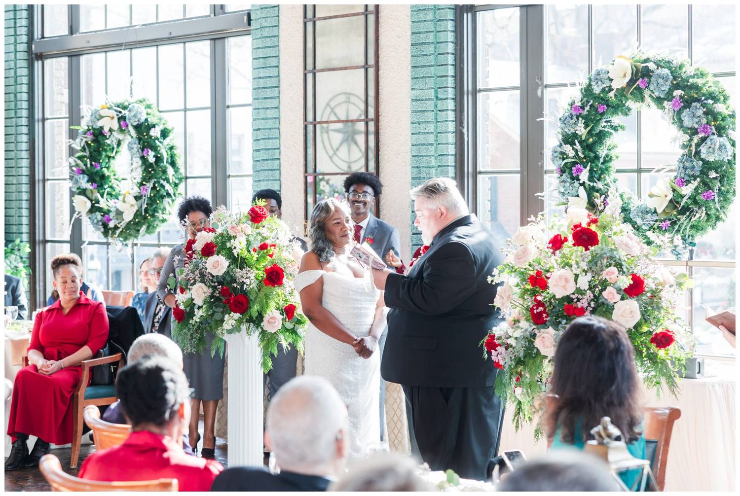 A panoramic view of a wedding reception in an elegant venue decorated with Christmas wreaths and red flowers.
