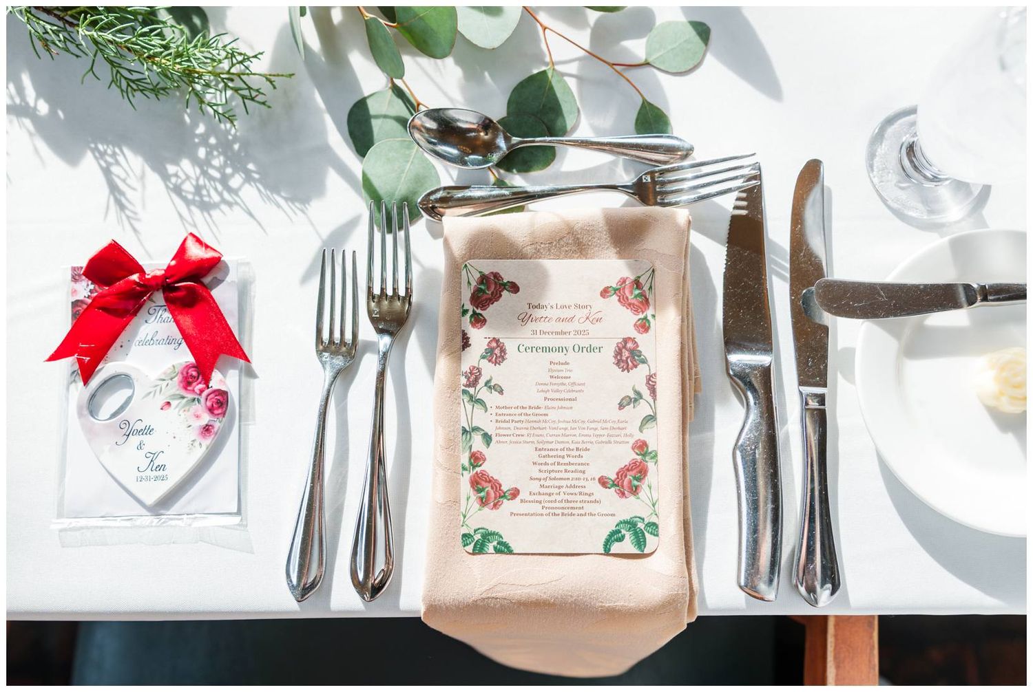 Holiday place settings with silver cutlery, red bows, and festive menu cards arranged on a white tablecloth.